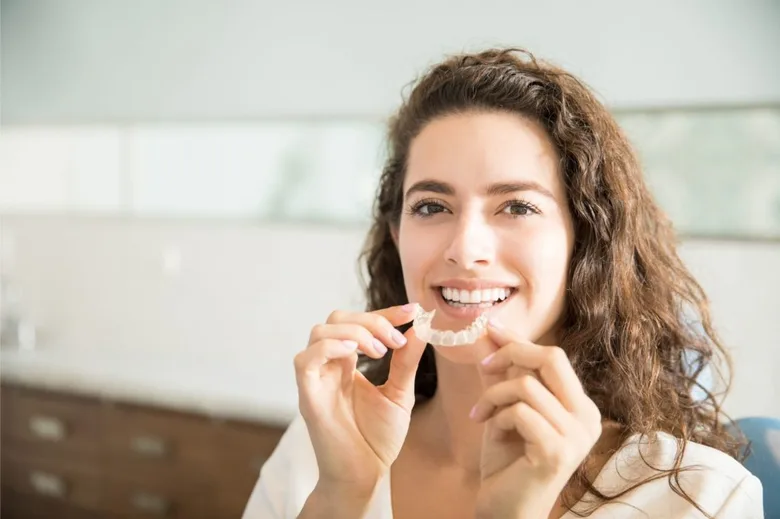 Smiling woman holding a clear Invisalign aligner