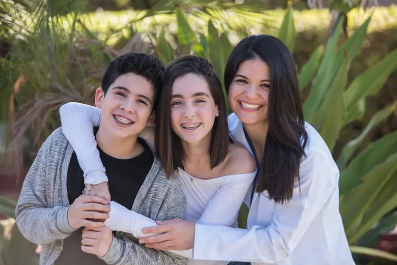 Smiling children with braces and an orthodontist in Miami, surrounded by greenery, promoting Miami Orthodontic Specialists' family-friendly care.