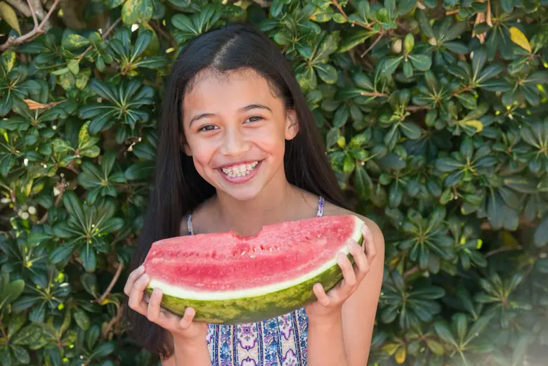 Child smiling and holding a watermelon slice with braces