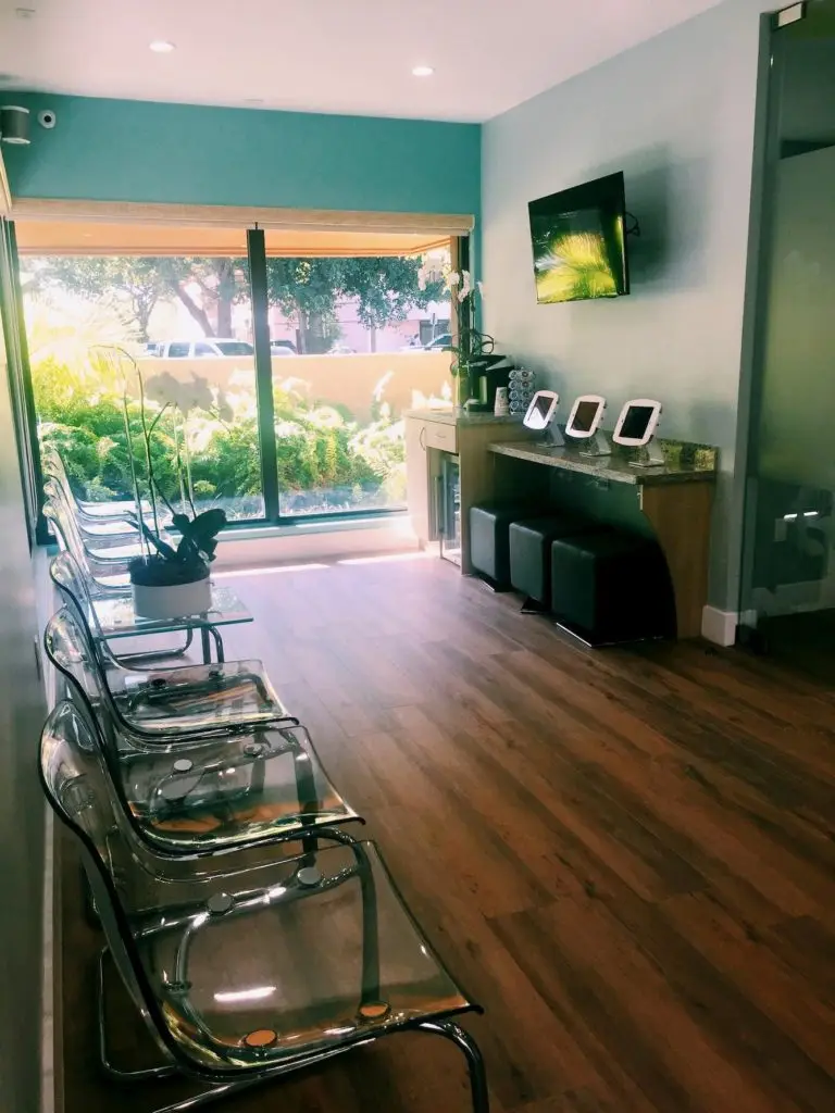 Modern orthodontic waiting area at Miami Orthodontic Specialists featuring clear chairs, a view of greenery, and a television, emphasizing a comfortable environment for braces and Invisalign patients.