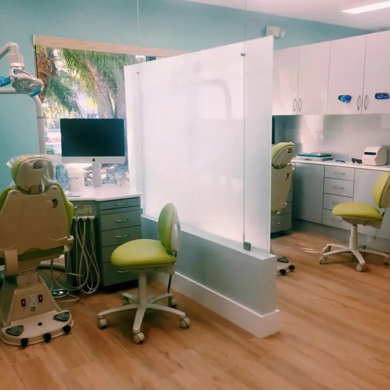Modern orthodontic treatment room at Miami Orthodontic Specialists, featuring privacy dividers, green dental chairs, and a computer workstation, emphasizing a comfortable environment for braces and Invisalign adjustments.